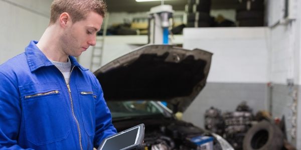 Mechanic holding tablet in front of vehicle